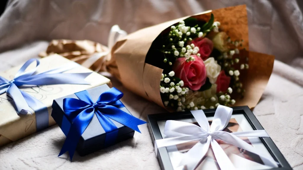 A beautifully wrapped assortment of thoughtful gifts including jewelry, flowers, and a personalized photo frame arranged on a soft blanket